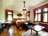Pokoj Vlasta Burian - prostorný pokoj s dřevěným nábytkem zdobeným kovovými prvky stojícím na původní dřevěné podlaze.
